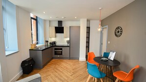 A modern kitchen with a central island, a dining area with colorful chairs, and a clock on the wall. - Spacious 2BED Central Manchester Flat w Security (Salford)