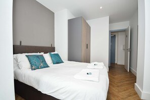 Ein modernes Hotelzimmer mit einem großen Bett, einem hölzernen Kopfteil und Blick auf einen Flur.
