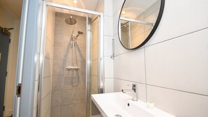 A modern bathroom with a glass-enclosed shower, a white sink, and a round mirror. - Spacious 2BED Central Manchester Flat w Security (Salford)