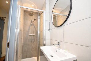 Ein modernes Badezimmer mit einer gläsernen Dusche, einem weißen Waschbecken und einem runden Spiegel.