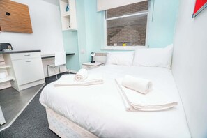 Ein Hotelzimmer mit Bett, Schreibtisch, Stuhl, Nachttisch und Fenster mit Blick auf eine Ziegelwand.