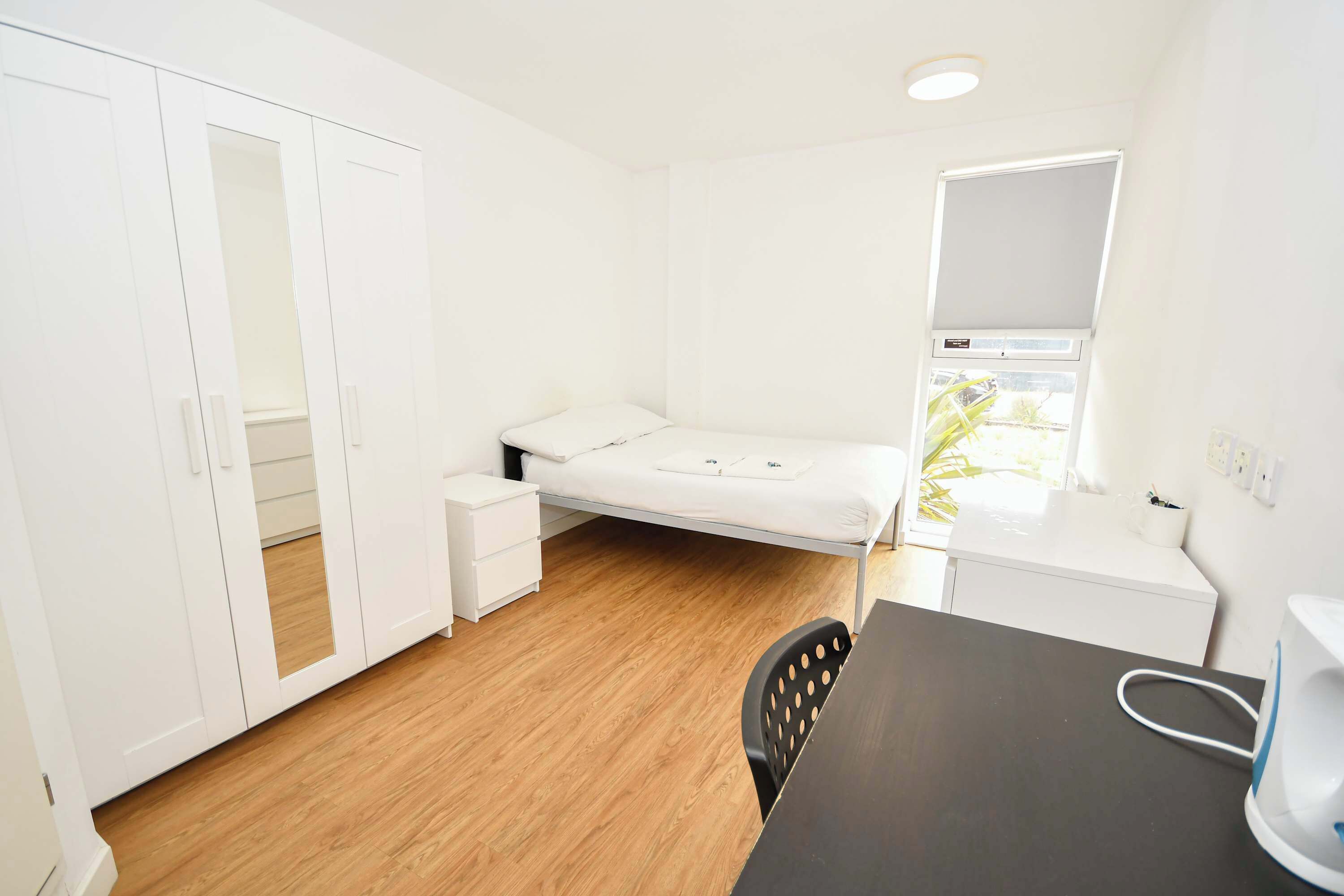 Una habitación pequeña y limpia con cama, escritorio, silla y armario.