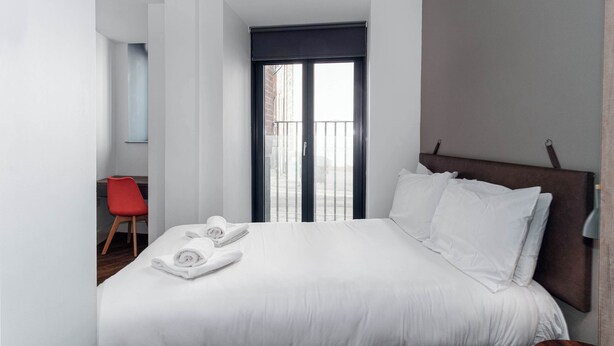Habitación de hotel con una cama, una silla roja y vistas al exterior.