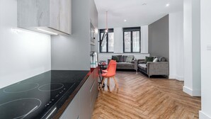 Una cocina moderna con estufa negra, un comedor con una silla roja y un sofá gris en la sala.