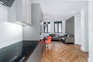 Eine moderne Küche mit einem schwarzen Herd, ein Essbereich mit einem roten Stuhl und ein graues Sofa in einem Wohnzimmer.