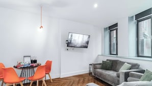 Una sala de estar moderna con un televisor de pantalla plana montado en la pared, un sofá gris, sillas naranjas y un piso de madera en patrón de espiga.