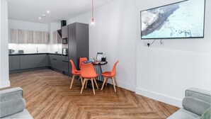 Una cocina moderna con armarios grises, un comedor con sillas naranjas y un televisor de pantalla plana montado en la pared.