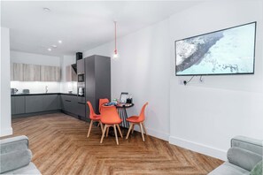 Eine moderne Küche mit grauen Schränken, ein Essbereich mit orangefarbenen Stühlen und ein an der Wand befestigter Flachbildschirm.