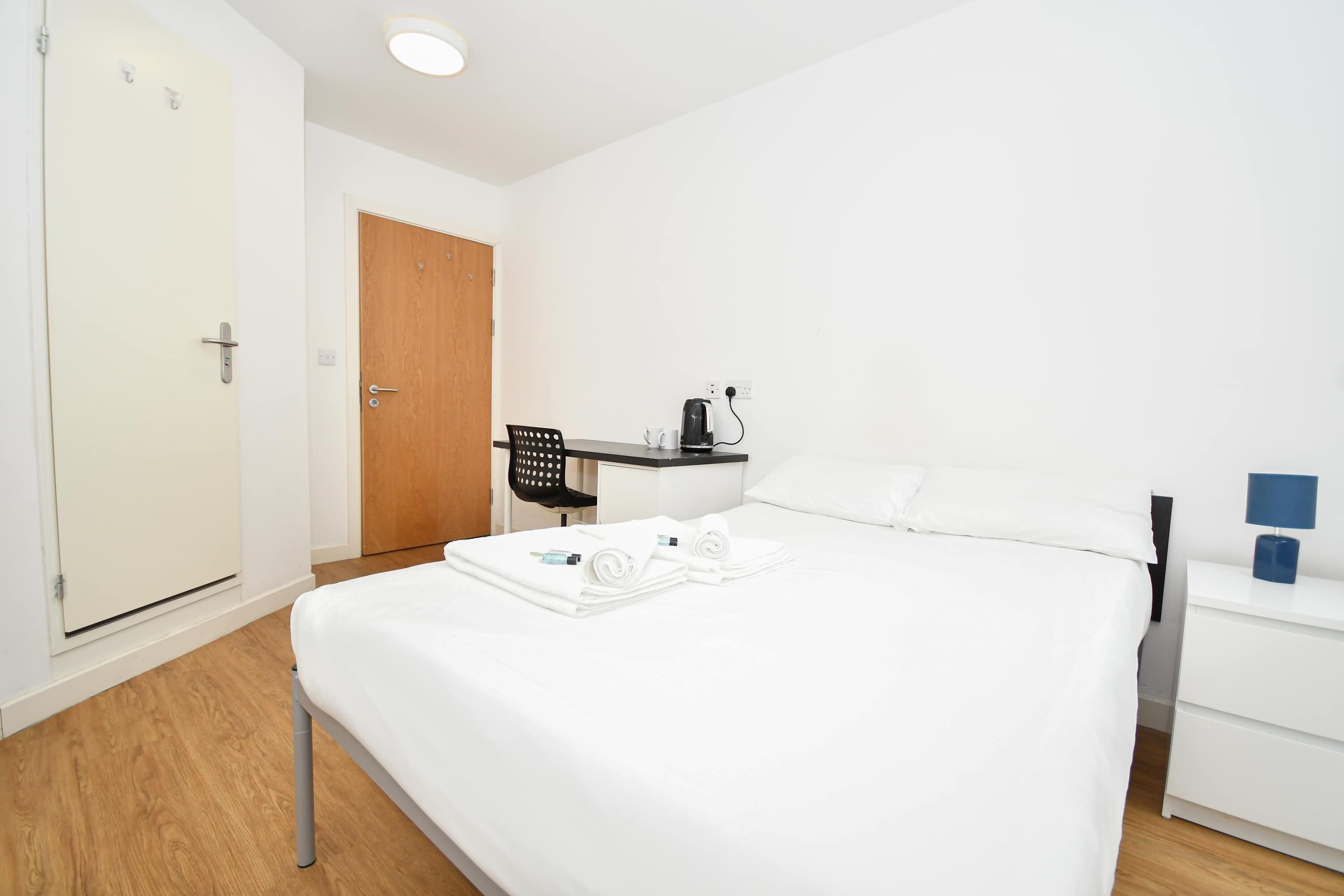 Hotellihuone, jossa on sänky, työpöytä, tuoli, vaatekaappi ja yöpöytä.