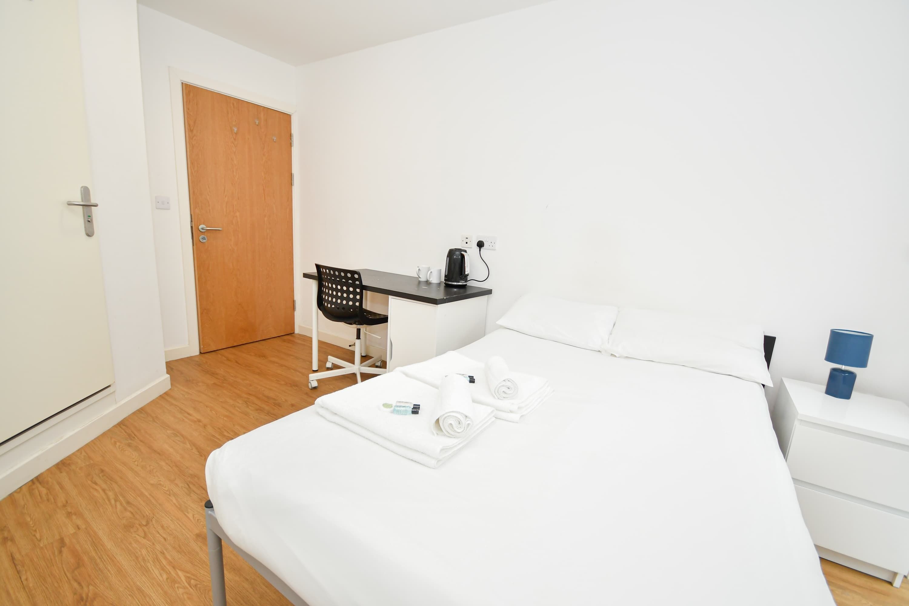 A hotel room with a bed, a desk, a chair, and a nightstand.