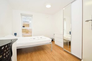 Een slaapkamer met een bed, een raam, een spiegel en een kledingkast.