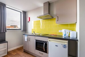 A compact kitchen with a microwave, oven, and dishwasher, a window with curtains, and a yellow backsplash. - Modern Budget Studio Apartment in Sheffield Centre (Sheffield)