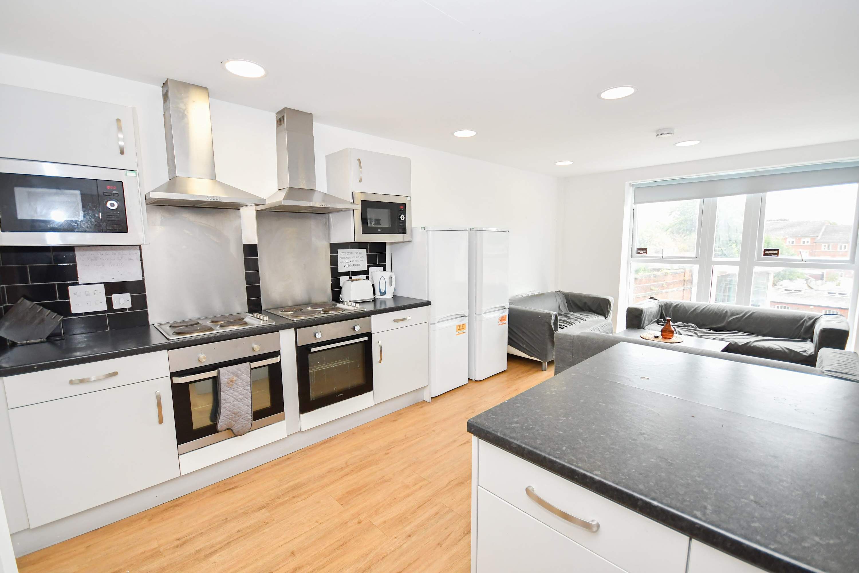 A modern kitchen with white cabinets, a stove, oven, microwave, and a large window.