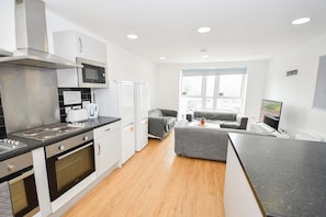 Eine moderne Küche mit Mikrowelle, Backofen und Kühlschrank. Im Wohnbereich befindet sich ein graues Sofa und ein Flachbildfernseher.