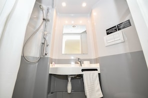 Ein kleines Badezimmer mit Dusche, Waschbecken und Spiegel.
