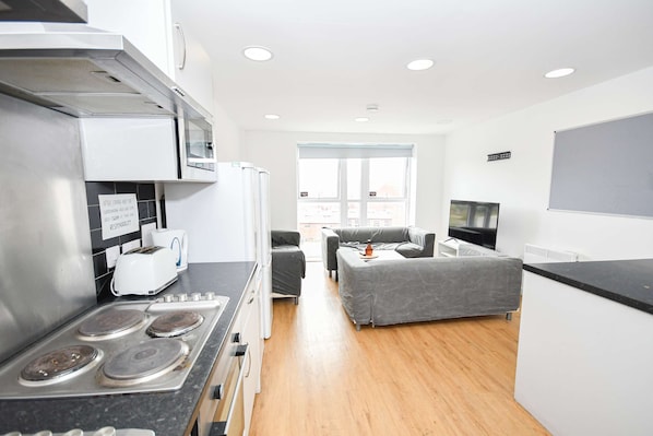 A modern kitchen with a stove, toaster, and refrigerator. There is a seating area with a sofa and a TV. - Modern & Convenient 4 Bed Apartment in Liverpool (Liverpool)