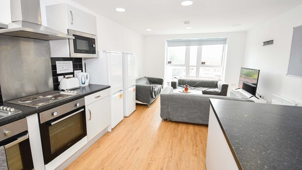 Een moderne keuken met een magnetron, oven en broodrooster, een grijze bank en een groot raam.