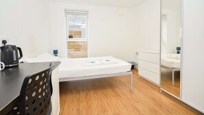 Een kamer met een bed, een bureau, een stoel, een raam en een spiegel.