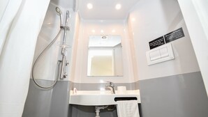 Een kleine badkamer met een douche, wastafel en spiegel.
