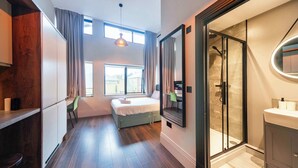 Ett modernt hotellrum med en säng, en dusch, en toalett med handfat och en matplats.