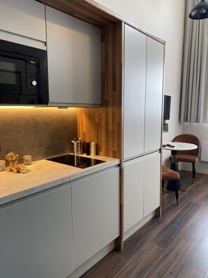 A modern kitchen with a built-in microwave, a sink, and a wooden accent wall. - Contemporary Studio in Central Hastings Near Beach (East Sussex)