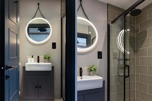 Un baño moderno con dos lavamanos, cada uno con un espejo redondo e iluminación debajo del mueble.