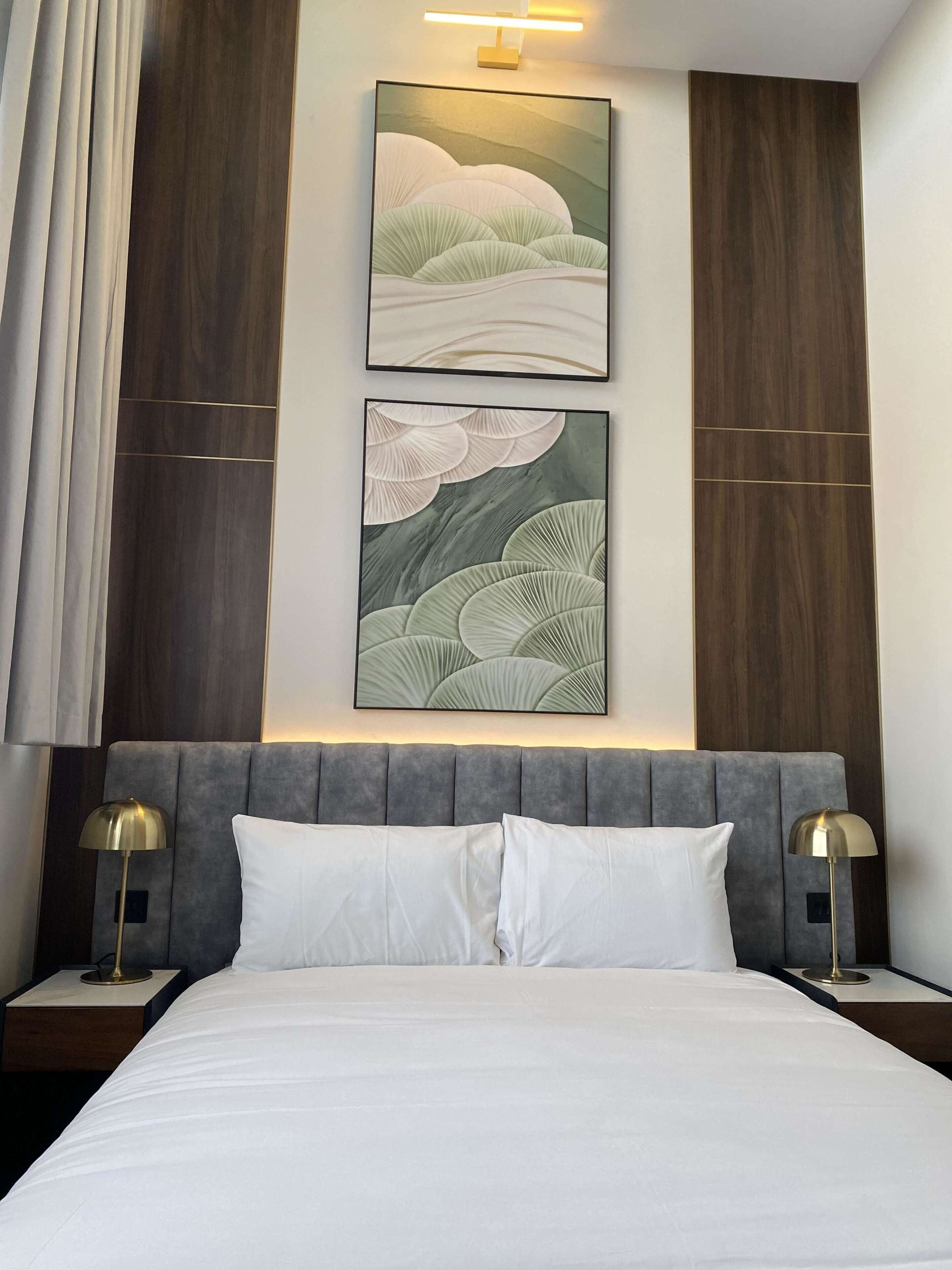 A hotel room with a bed, two bedside lamps, a headboard, and two framed artworks on the wall.