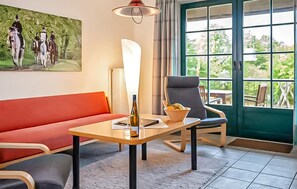 A room with a red sofa, a wooden table with a bottle, a bowl of fruit, and a chair. - 2 bedroom stunning apartment in Ribnitz-Damgarten (Ribnitz-Damgarten)