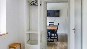 Een gang met een houten kruk, een witte deur, en een eethoek met een tafel en stoelen.
