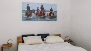 Een slaapkamer met een bed, twee nachtkastjes en een schilderij van paarden aan de muur.