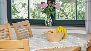 A wooden chair, a table with a placemat, a bowl of fruit, and a vase with flowers by a window. - Cozy apartment in Ribnitz-Damgarten with house a panoramic view (Ribnitz-Damgarten)