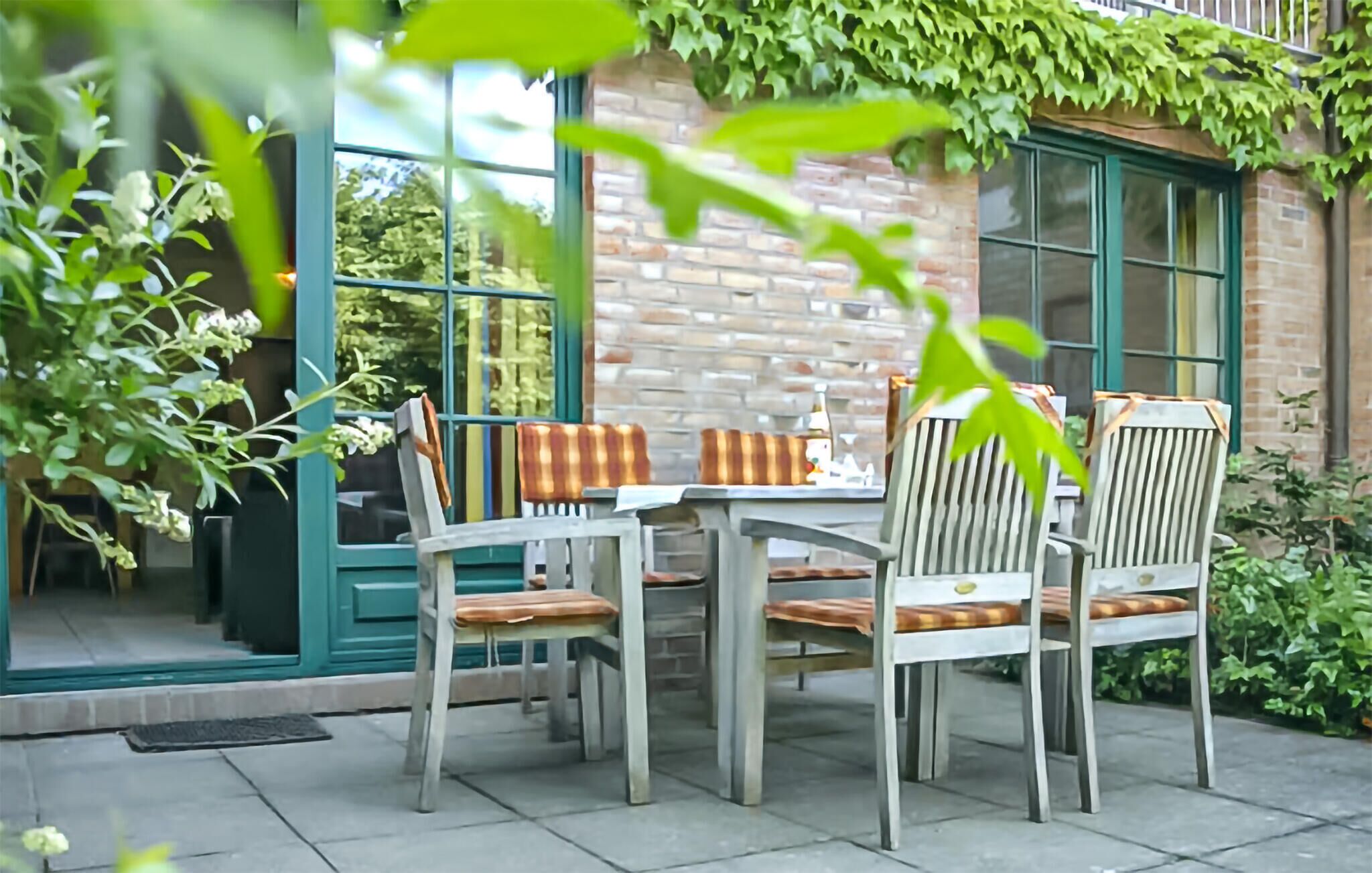 An outdoor patio with a table and chairs, a brick wall, and greenery.