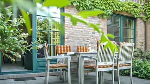 An outdoor patio with a table and chairs, a brick wall, and greenery. - Cozy apartment in Ribnitz-Damgarten with house a panoramic view (Ribnitz-Damgarten)