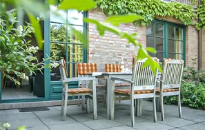 Eine Terrasse im Freien mit Tisch und Stühlen, einer Ziegelwand und viel Grün.