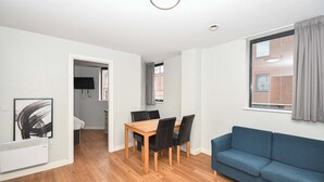 A modern apartment with a dining area, a blue sofa, and a view of a building through a window. - Spacious Budget 3-Bed Sheffield Centre Apt (Sheffield)