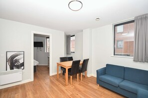 Ein modernes Apartment mit Essbereich, einem blauen Sofa und Blick auf ein Gebäude durch ein Fenster.