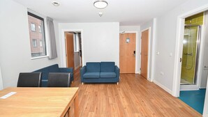 A room with a wooden floor, a blue sofa, a wooden table, and a door leading to a bathroom with a shower. - Spacious Budget 3-Bed Sheffield Centre Apt (Sheffield)