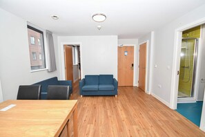 Ein Zimmer mit Holzboden, einem blauen Sofa, einem Holztisch und einer Tür zu einem Badezimmer mit Dusche.