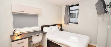 Une chambre à coucher comprenant un lit, un bureau, une chaise et un téléviseur fixé au mur.