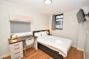 Ein Schlafzimmer mit Bett, Schreibtisch, Stuhl und einem an der Wand befestigten Fernseher.