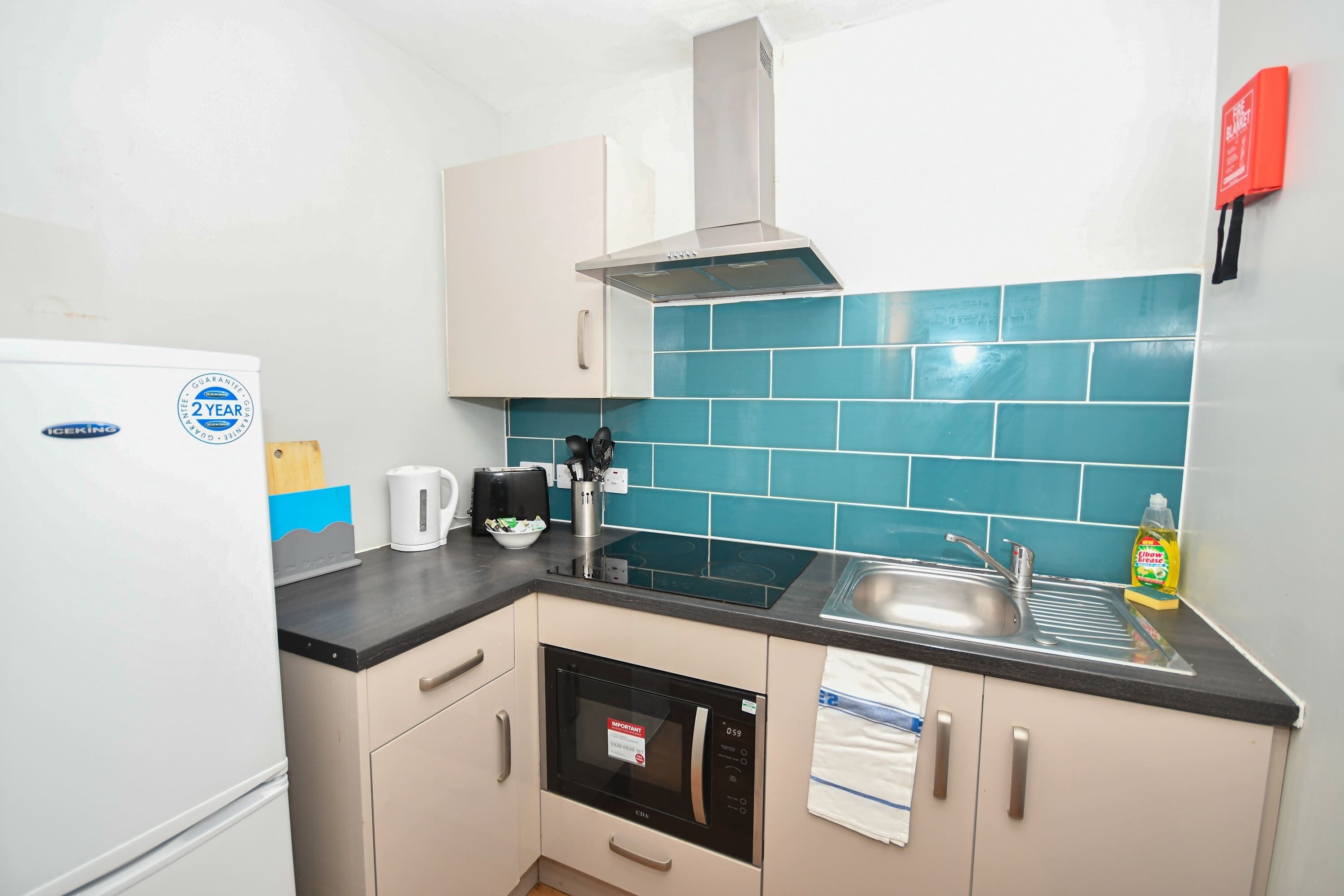 A compact kitchen with a refrigerator, microwave, stove, and sink.