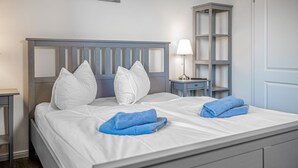 Un letto rifatto con cura, lenzuola e cuscini bianchi, un asciugamano blu, una lampada da comodino e un piccolo comodino con una lampada.