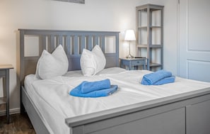 A neatly made bed with white bedding and pillows, a blue towel, a bedside lamp, and a small nightstand with a lamp. - 1 bedroom amazing apartment in Barth (Barth)