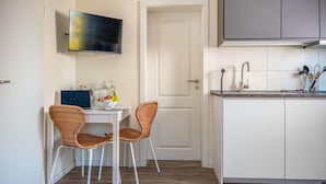 Una cucina compatta con zona pranzo, una TV montata sopra il tavolo e una porta che dà su un'altra stanza.