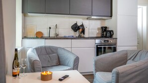 Ett modernt kök med grå skåp, en kaffebryggare och en mikrovågsugn. Det finns två grå fåtöljer och ett bord med ett ljus och en fjärrkontroll.