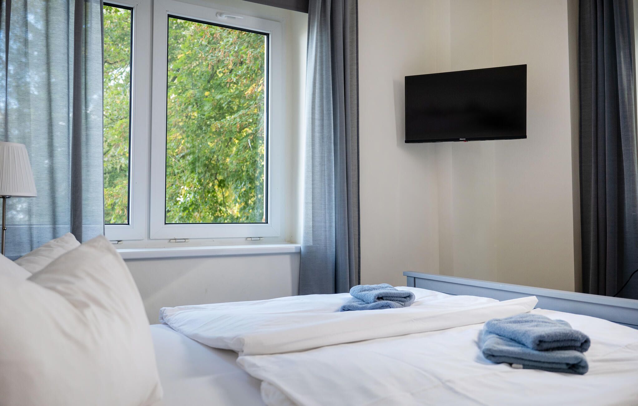 Een hotelkamer met een bed, een televisie aan de muur en een raam met gordijnen.