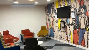 A room with a modern design, featuring a flat-screen TV mounted on the wall, a variety of colorful chairs, and a patterned mural.