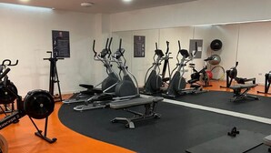 A gym with exercise equipment, a mirrored wall, and a black mat area.