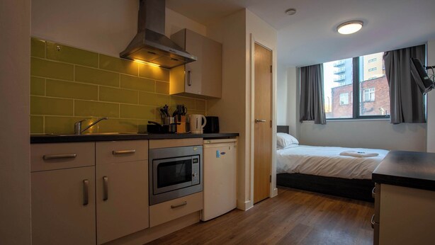A compact kitchen with a microwave, oven, and sink, a small refrigerator, and a window with curtains.