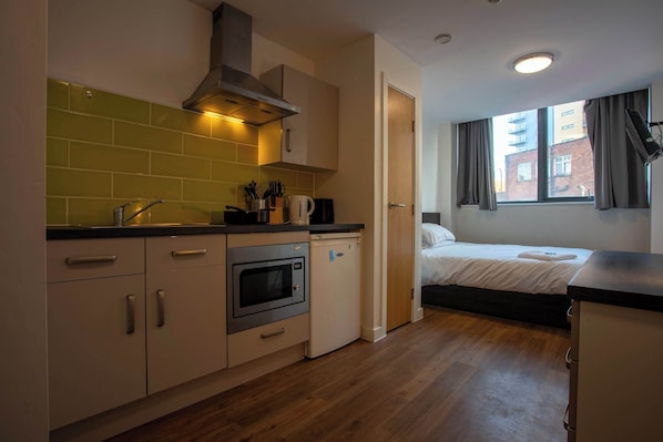 A compact kitchen with a microwave, oven, and sink, a small refrigerator, and a window with curtains.